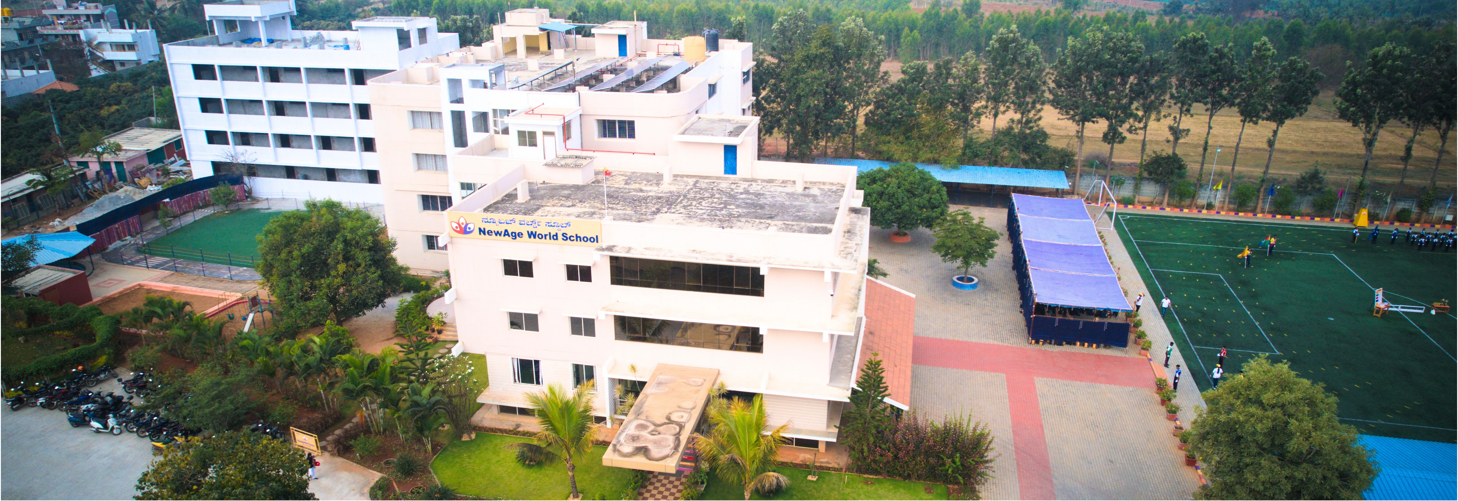 Aerial view of NewAge World School campus featuring modern buildings, lush greenery, and well-equipped sports facilities in Bangalore.
